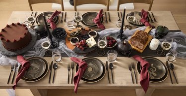 West Elm table setting with six chairs, red napkins, brown plates, a chocolate cake, bread, candlesticks, and berries.