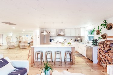 a large kitchen with an island flanked by metal stools, white cabinets, and a rustic pine floor