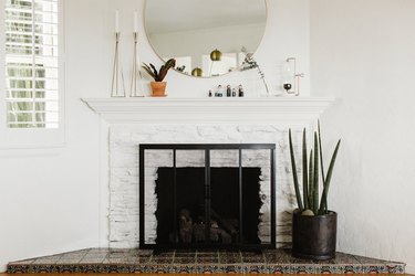 Large white brick fireplace with screen and large round mirror hanging above