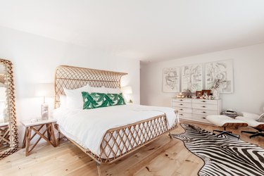 a bed with a rattan frame in a bedroom with pine floors and a zebra-skin rug