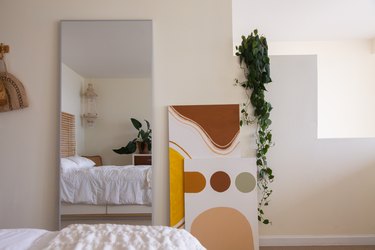 Full-length mirror next to neutral geometric art and a pothos plant on a stepped wall.