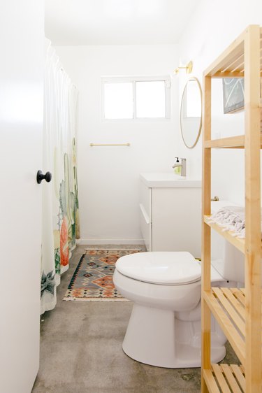 a long narrow bathroom with a concrete floor and a tall wooden shelving unit