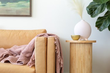 Fluted side table with dowel base, birch circle board tabletop, round pink vase and gold bowl, neutral sofa and pink blanket