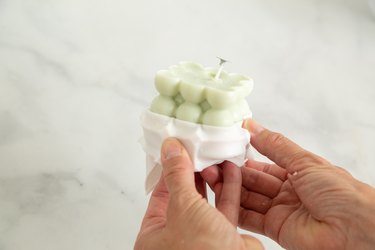 Person removing a pastel green, bubble cube candle from a plastic mold.