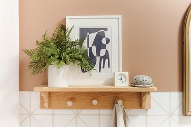 Wood shelf with a clay diffuser, white clock, framed abstract print, and fern plant.