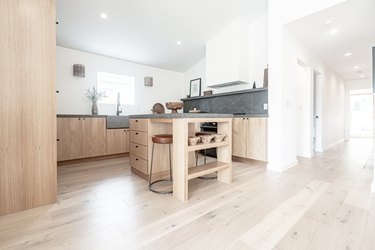 Minimalist kitchen with light wood floors, light wood cabinets, gray backsplash and kitchen island