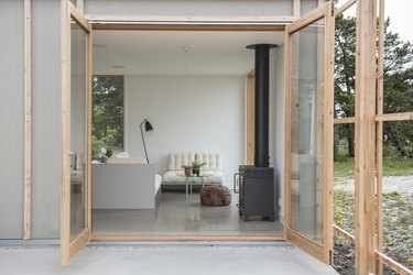 open french doors provide a view into the clean, uncluttered living room, including a wood-burning stove and white furniture