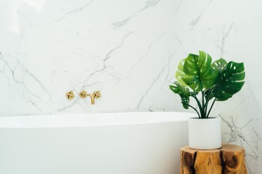 White marble walls with a freestanding bathtub, a rustic wood stool, and a potted monstera plant
