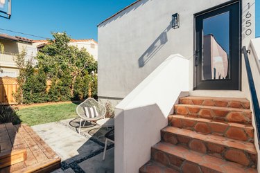 White house with terra-cotta tile roof and steps, outdoor furniture, and casement door