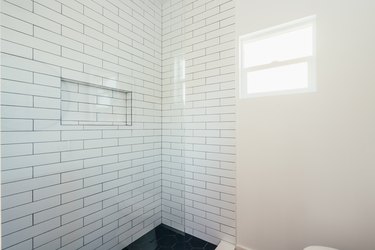 Corner of a shower with white subway tile, a niche, and black hexagonal tile floor