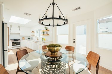 Glass tabletop dining table with modernist wood chairs and a black industrial chandelier