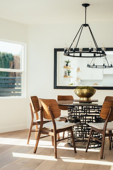 Dining room with wood modernist chairs, dining table, gold brass bowl, large square mirror, and industrialist chandelier