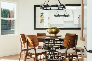 Dining room with wood modernist chairs, dining table, gold brass bowl, large square mirror, and industrialist chandelier