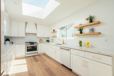 White kitchen cabinets with gold handles, skylight, wood flooring in a minimalist kitchen