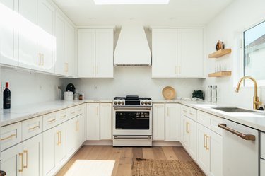 White cabinets with gold handles, wood dishware shelves and wood flooring in a minimalist kitchen