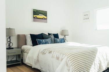 Bed with gray upholstered headboard, white bedding, blue-gray pillows, symmetrical table lamps and nightstands