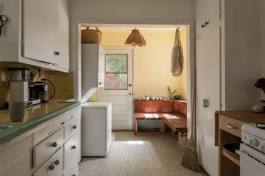 Kitchen with white cabinets and green-neutral tile counter. A wood bench with pottery and a floral shape pendant light.