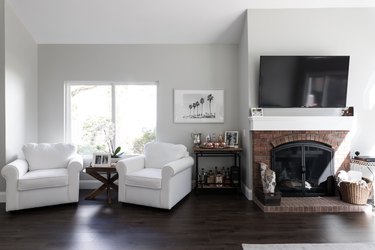 Living room with light grey walls with white millwork. White armchairs, brick fireplace, and a bar cart.