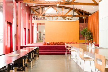 Red and yellow walls, wood beam ceiling with white fans, Red carpet with an indent with orange pillows. Dining furniture on either side.