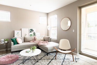 A bright living room with green, pink, white, and beige color theme, round accents, and foliage art.