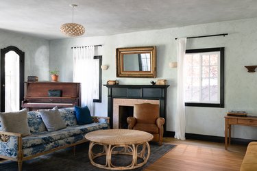 Living room with boho coffee table, fireplace, blue-white sofa, gold frame mirror, vintage piano, latticed pendant light, black frame windows