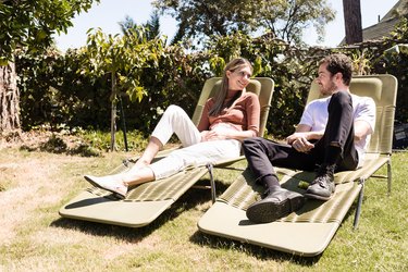 A man and a woman lounge on green plastic lawn chairs.