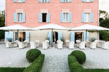 Exterior of two story brick hotel with light blue shutters and white outroor dining patio with large white umbrellas