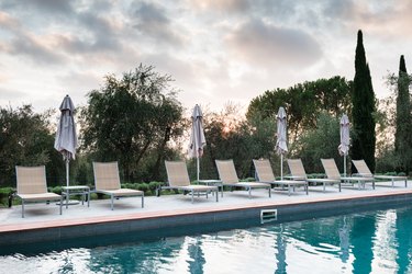 Pool side lounge chairs with closed umbrellas at dusk