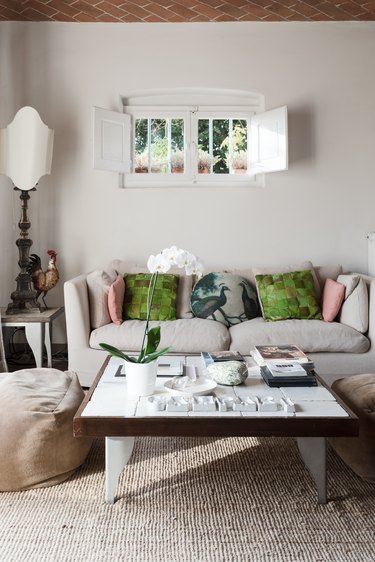 White love seat with green throw pillows under small window with white shutters