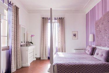 Lavender bedroom with upholstered headboard and lavender striped wallpaper