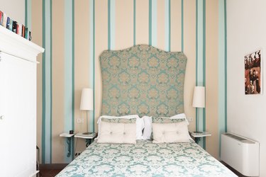 Green and cream bedroom with upholstered headboard and striped wallpaper