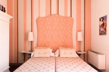 Rosy bedroom with pink and white striped wallpaper and fabric headboard