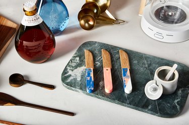Marble cutting board with knives, spice jar, wood spoons, bourbon, gold measuring spoons