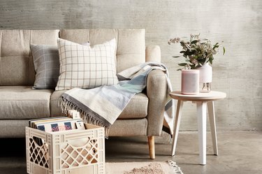 Neutral sofa with pillows and scarf next to side table with speaker and vase and crate of records