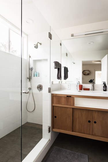 White bathroom with glass shower walls and brown cabinets