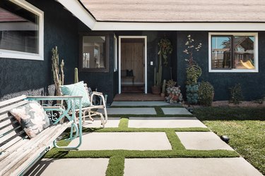 A backyard of a dark ranch house, with concrete pavers, a park bench, and a green lawn