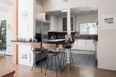 Wood kitchen island, with a black wire counter and brown bar stools. A Midcentury multi-sphere clock.