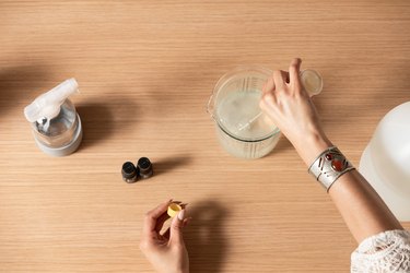 Hand holding eye dropper over measuring cup filled with liquid on wood countertop