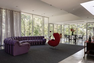 Living room with Midcentury furniture and full-glass windows. A purple leather sofa and a red winged egg chair.