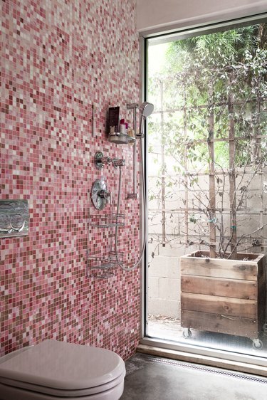 pink mosaic shower tile in an open shower, glass door leading to a back patio, white toilet