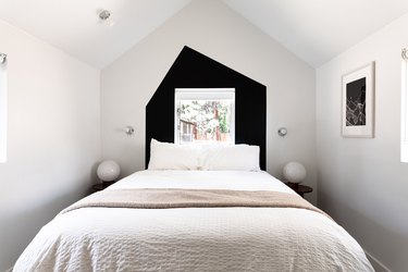 A minimalist white bedroom with black wall accent, globe lamps, and vaulted ceiling