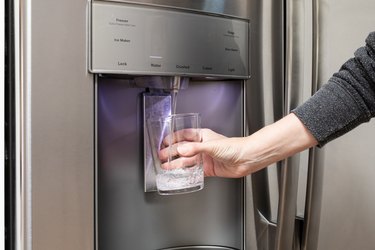 Water Dispenser from Dispenser of Home Fridge, Woman is Filling a