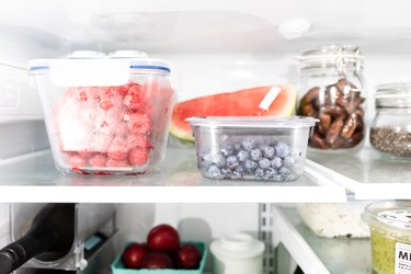 Raspberries and blueberries in clear glass containers on the top shelf in the refrigerator.