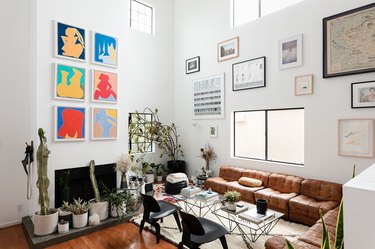 Living room with eclectic wall art, leather sofas, black Midcentury chairs, glass coffee tables, and plants.