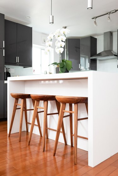 White kitchen island with wood stools and an orchid plant