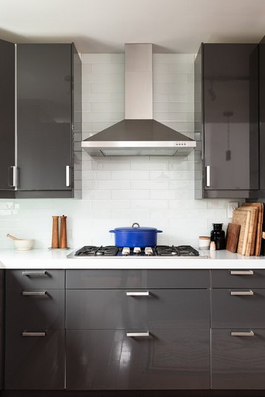 Kitchen with gray cabinets and white tile backsplash, stove with a blue cast iron pot, and kitchen wares on the counters.