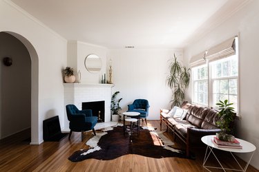 Living room with blue tufted accent chairs, leather sofa, white mantel fireplace, animal skin rug, and round accents.