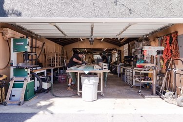 An open garage door, with two people working at woodworking tables.
