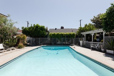 Swimming pool with white patio furniture, plants in planters, and a white pergola.