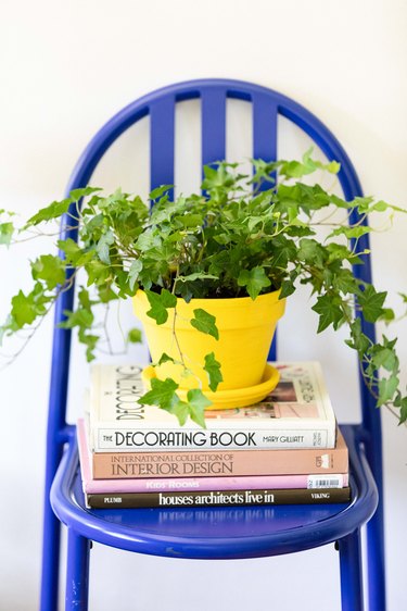 A bright blue chair with a stack of interior design and architecture books and a plant in a yellow planter
